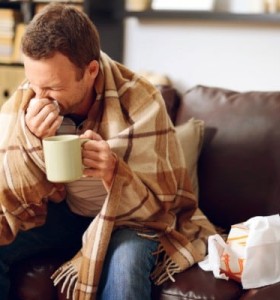 Man wrapped in a blanket blowing his nose.