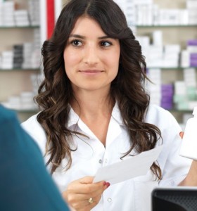 Pharmacist with long dark hair assisting customer in dark green shirt