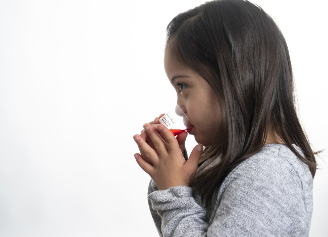 Racially ambiguous girl with dark hair drinking liquid medicine against white background