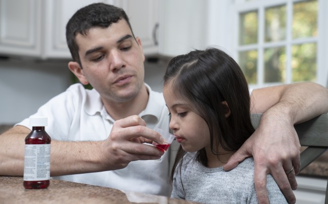 Caucasian/White man giving racially ambiguous young girl liquid medicine