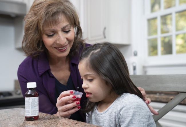 Hispanic/Latinx woman giving Hispanic/Latinx young girl liquid medicine