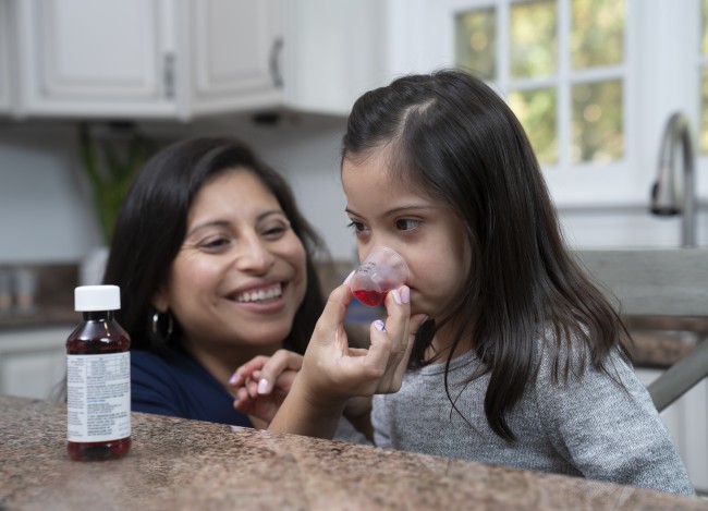 Hispanic/Latinx woman giving Hispanic/Latinx young girl liquid medicine