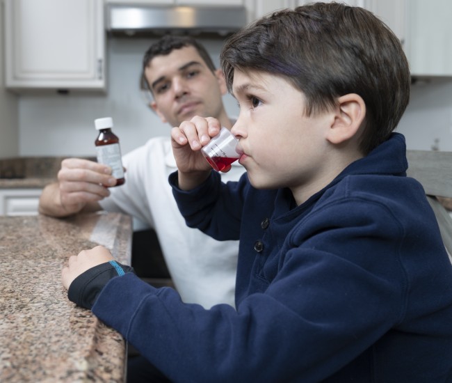 Caucasian/White man giving racially ambiguous boy liquid medicine