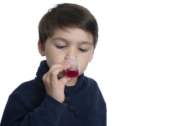 Hispanic/Latinx young boy drinking medicine against white background