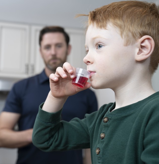 Caucasian/White man giving Caucasian/White boy liquid medicine