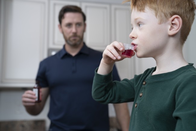 Caucasian/White man with beard giving Caucasian/White boy liquid medicine