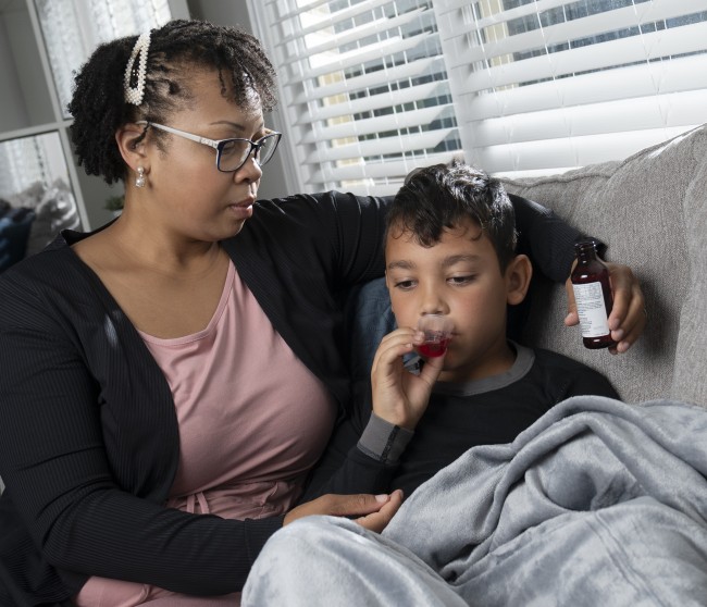 African American/Black woman giving sick Hispanic/Latinx boy liquid medicine