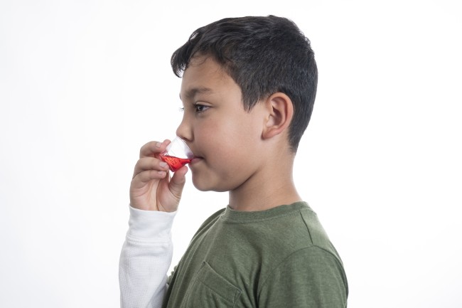 Hispanic/Latinx Boy in green shirt drinking medicine against white background