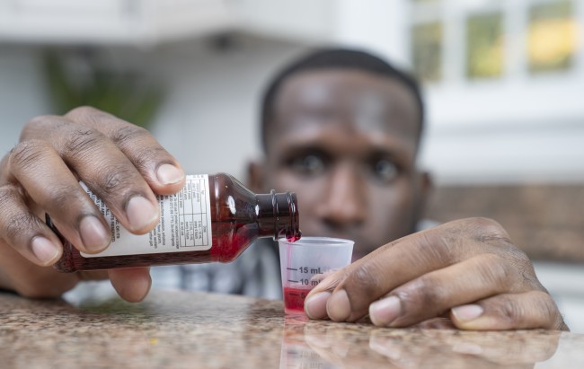 African American/Black man measuring liquid medicine