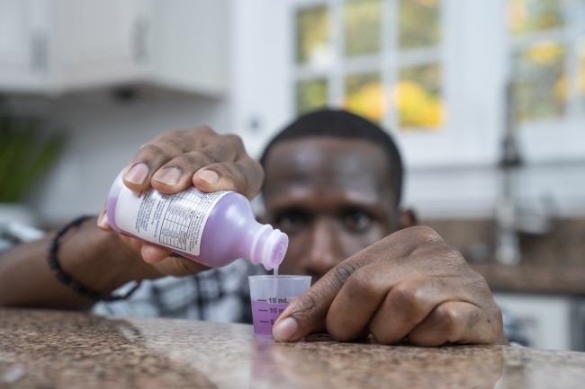 African American/Black man measuring liquid medicine