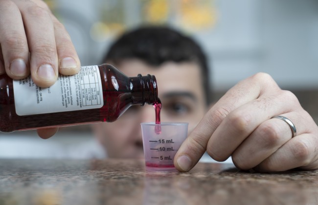 Caucasian/White man with dark hair measuring liquid medicine