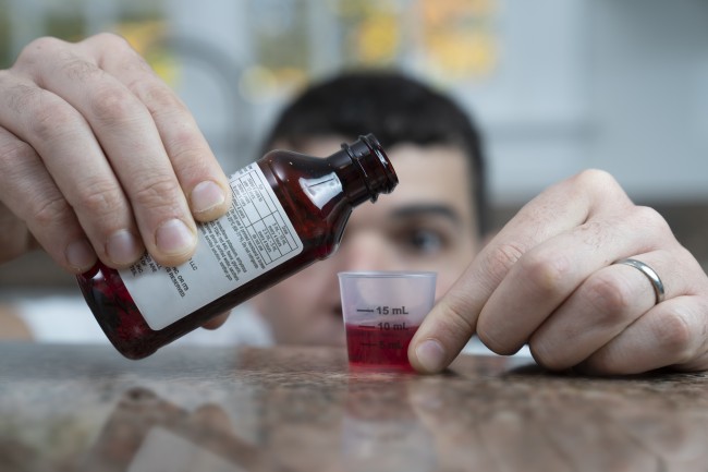 Caucasian/White man with dark hair measuring liquid medicine