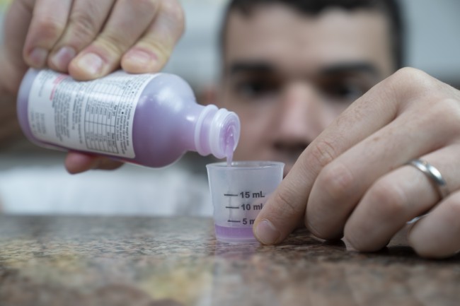 Caucasian/White man with dark hair measuring liquid medicine