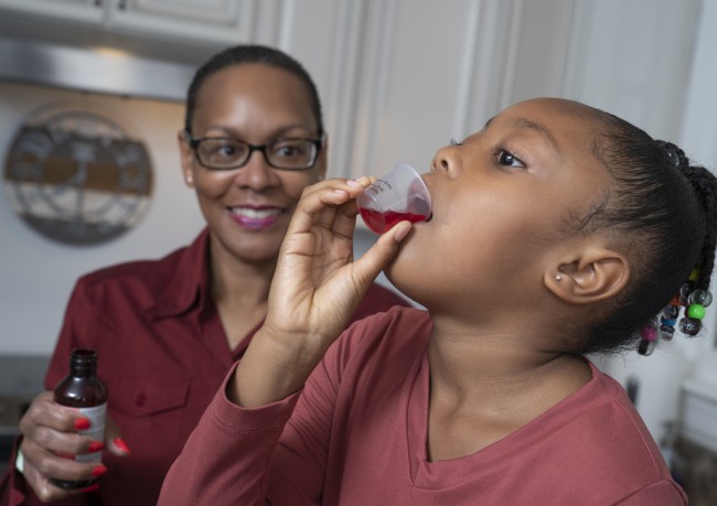 African American/Black woman in glasses giving African American/Black girl liquid medicine