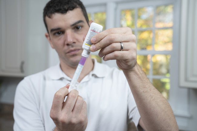 Caucasian/White man with dark hair measuring liquid medicine with syringe