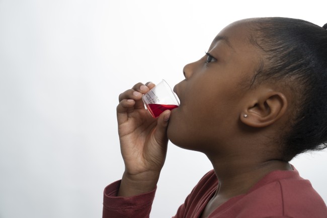 African American/Black girl in red shirt drinking liquid medicine against white background