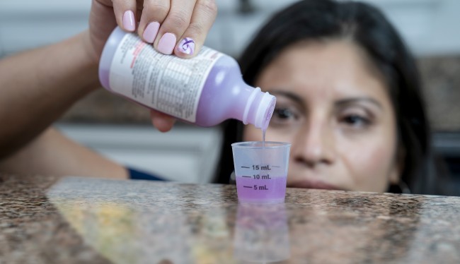 Hispanic/Latinx woman with dark hair measuring liquid medicine