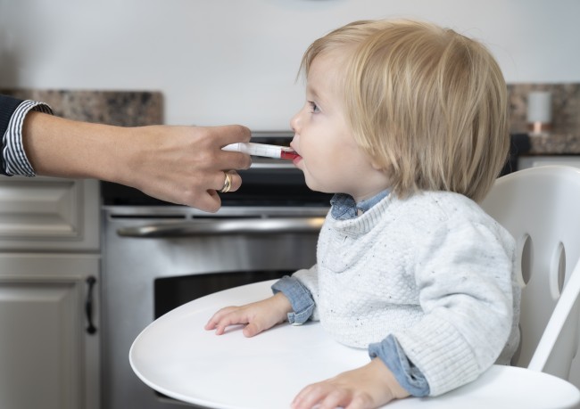 Caucasian/White toddler with blonde toddler in high chair being given liquid medicine