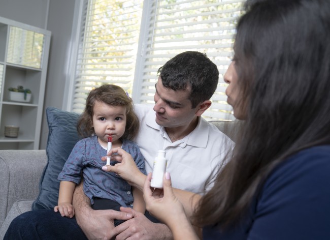 Racially ambiguous man and woman giving racially ambiguous toddler medicine