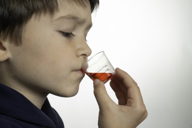 Profile view of Hispanic/Latinx young boy drinking medicine against white background