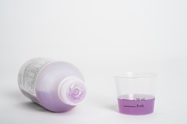 Liquid medicine bottle on its side and dosing cup with purple medicine