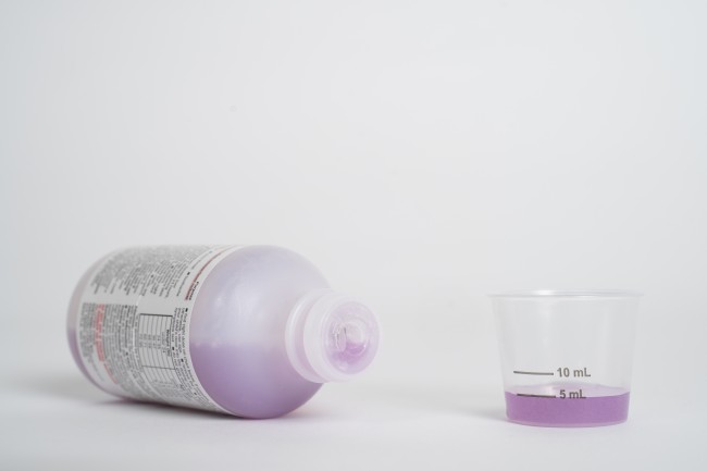 Liquid medicine bottle on its side and dosing cup with purple medicine
