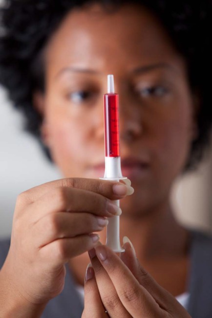 African American/Black woman measuring liquid medicine with syringe