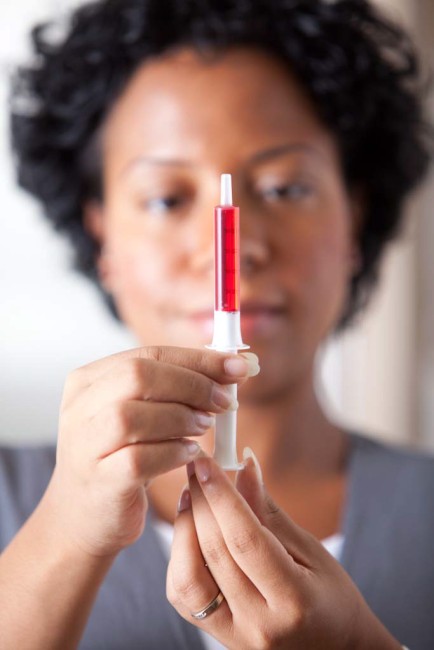 African American/Black woman measuring liquid medicine with syringe