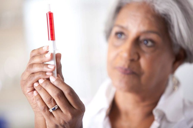 African American/Black older woman measuring red liquid medicine with dosing syringe