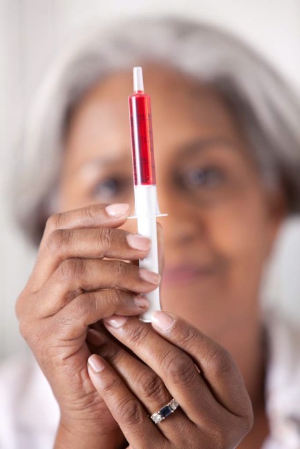 African American/Black older woman measuring red liquid medicine with dosing syringe