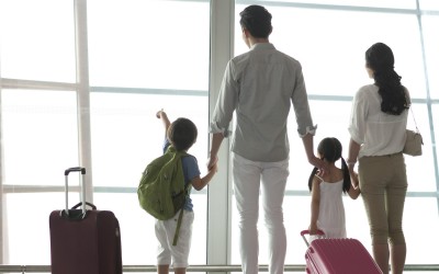 family with suitcases facing away looking out a window