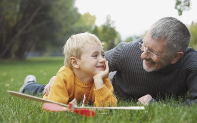 grandfather and grandchild laying on grass with a toy airplane