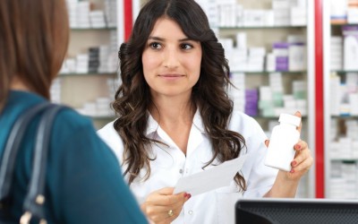 Pharmacist with long dark hair assisting customer in dark green shirt