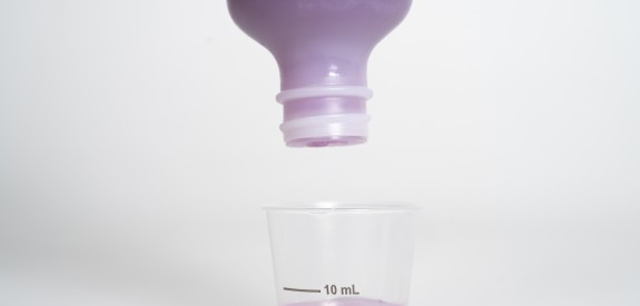 Purple liquid medicine being poured into dosing cup