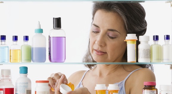 Hispanic woman measuring out medicine in front of a medicine cabinet
