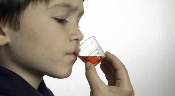 Profile view of Hispanic/Latinx young boy drinking medicine against white background