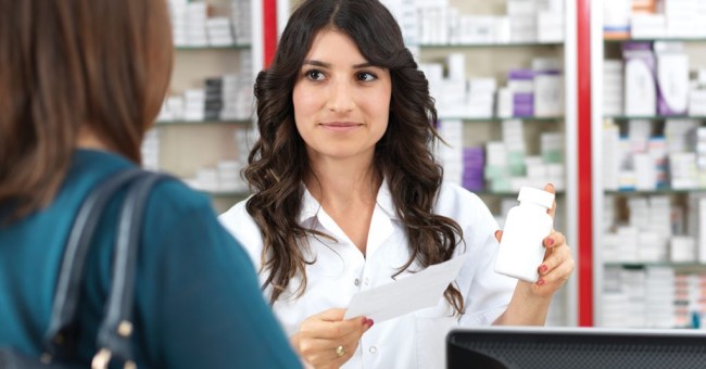 Pharmacist with long dark hair assisting customer in dark green shirt