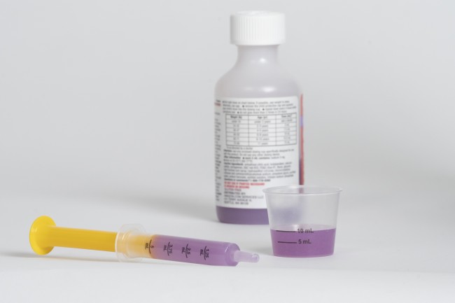 Medicine bottle, syringe, and dosing cup with purple liquid medicine