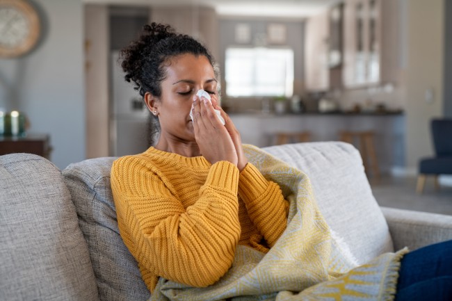 African American woman wearing a yellow sweater blowing her nose